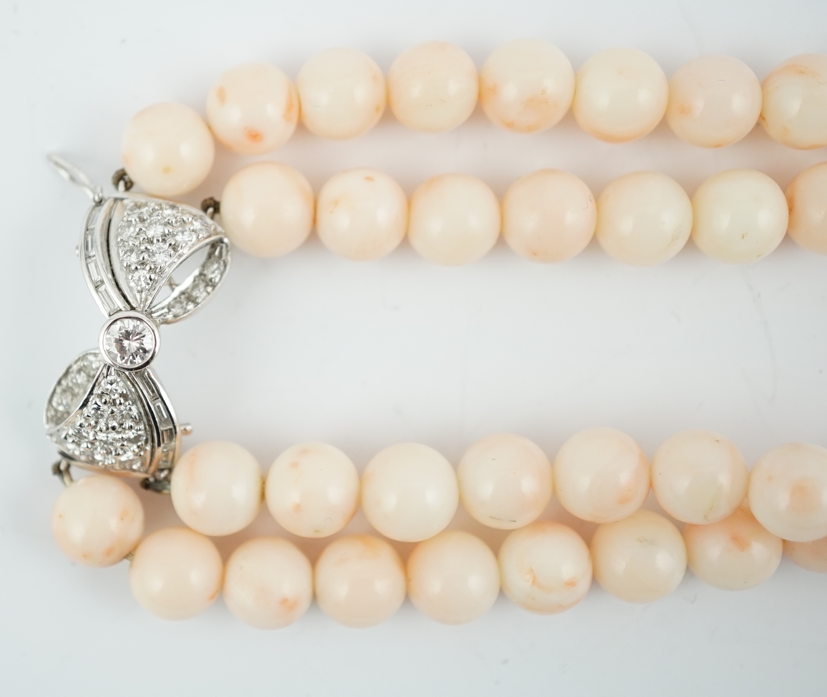 A double strand pale pink coral bead choker necklace, with round and baguette cut diamond cluster set bow shaped 18k white gold clasp